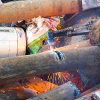 A worker uses a oxygen acetylene cutting torch to cut scrap at twilight